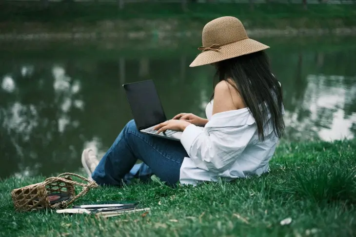 Travailleuse indépendante assise dans l’herbe avec un ordinateur portable